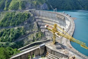 A yellow crane standing on a large curved concrete dam under construction