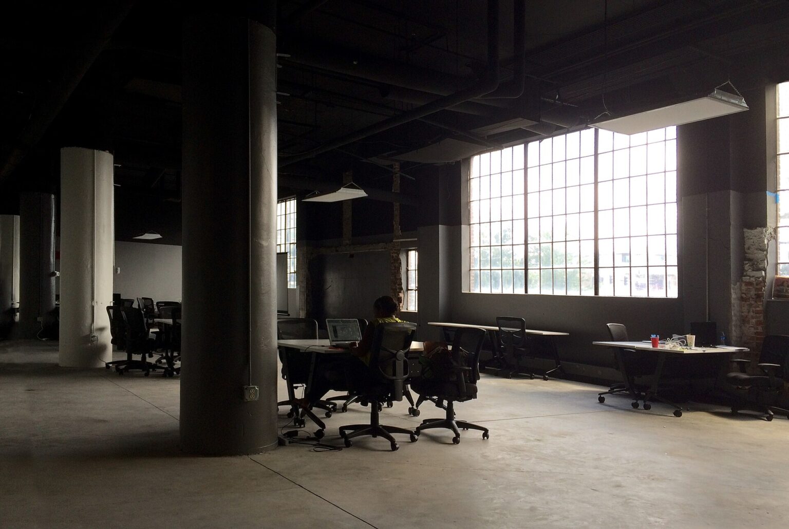 One person working alone at a laptop in a large, mostly empty open-plan office